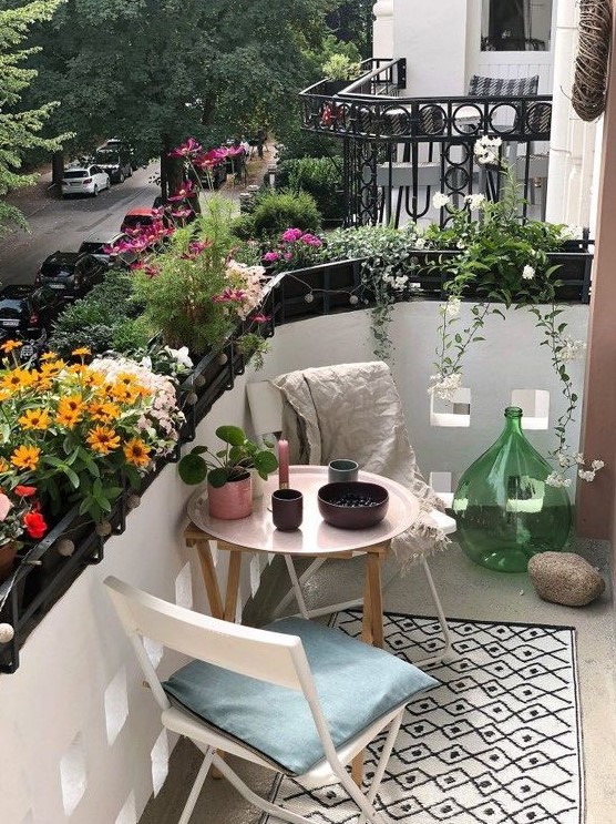 a tiny summer balcony with lots of potted blooms, wooden and metal furniture and pretty accessories