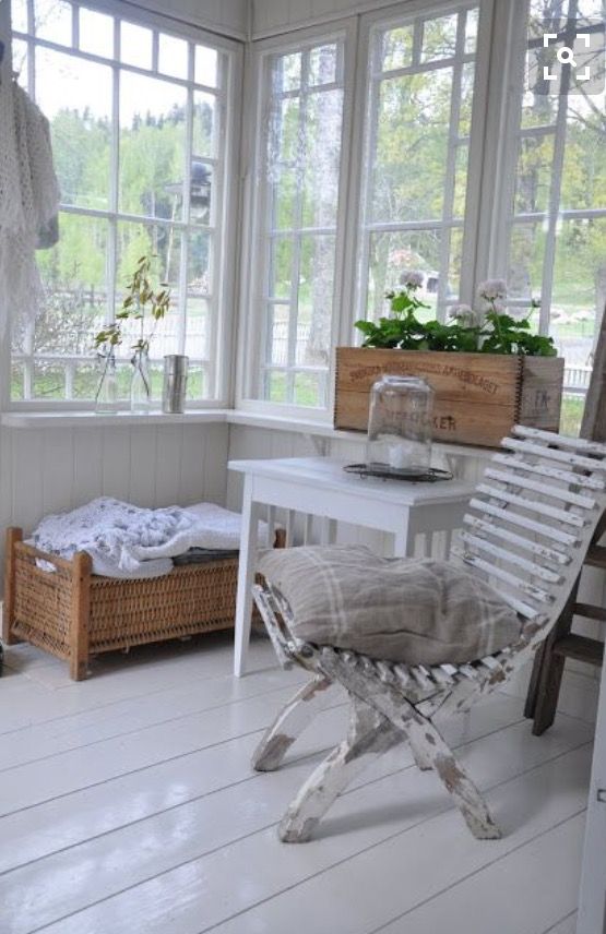 a vintage and shabby chic Scandinavian sunroom with vintage white furniture, a woven bench and a crate with blooms