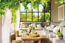 a welcoming Mediterranean terrace with a built-in corner sofa, a low wooden table, baskets, lanterns and greenery and blooms