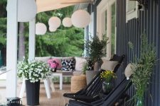 a welcoming Scandinavian porch with black wooden chairs with pillows, blooms and greenery, a tan sofa and a table