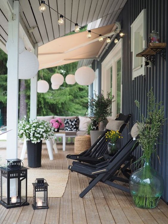 a welcoming Scandinavian porch with black wooden chairs with pillows, blooms and greenery, a tan sofa and a table
