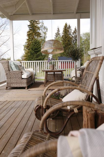 a welcoming Scandinavian porch with wicker chairs, a table and a woven pendant lamp plus rattan chairs and a stump