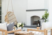 a welcoming modern farmhouse terrace with a fireplace, neutral upholstered furniture, a duo of side tables and a pendant chair