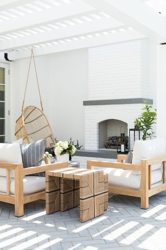a welcoming modern farmhouse terrace with a fireplace, neutral upholstered furniture, a duo of side tables and a pendant chair