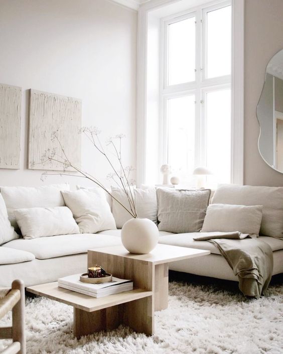 an airy and chic neutral living room with a creamy sectional, a catchy plywood coffee table, a mini gallery wall and a cool round vase