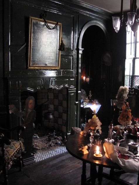 an elegant Gothic living room with black walls, a fireplace, artworks, a chandelier and a table with crystals and flowers