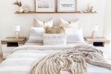 an ethereal neutral bedroom with wooden nightstands, a bed, an open shelf, pampas grass and artworks