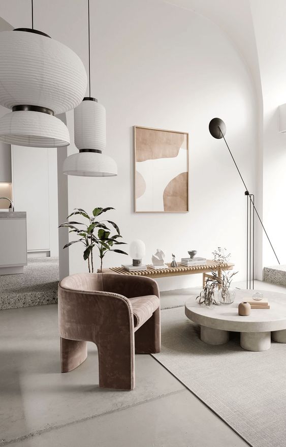 an exquisite neutral living room with a wooden bench used fro displaying, a low round coffee table, a dusty pink chair and pendant lamps