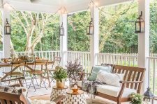 an inviting modern farmhouse terrace with white upholstered furniture, mini side tables, a wooden dining set, some fall decor