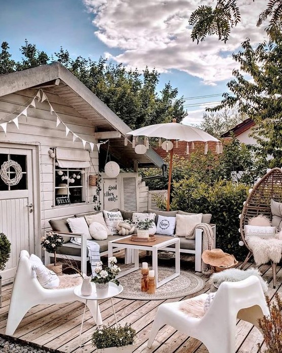 an inviting summer terrace with chic outdoor furniture, an egg-shaped chair, white plastic chairs, candles, an umbrella and potted plants and blooms