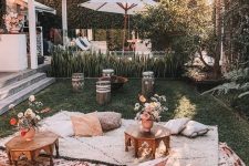 an outdoor boho space with layered neutral rugs, cushions and pillows, low carved tables, patterned stools