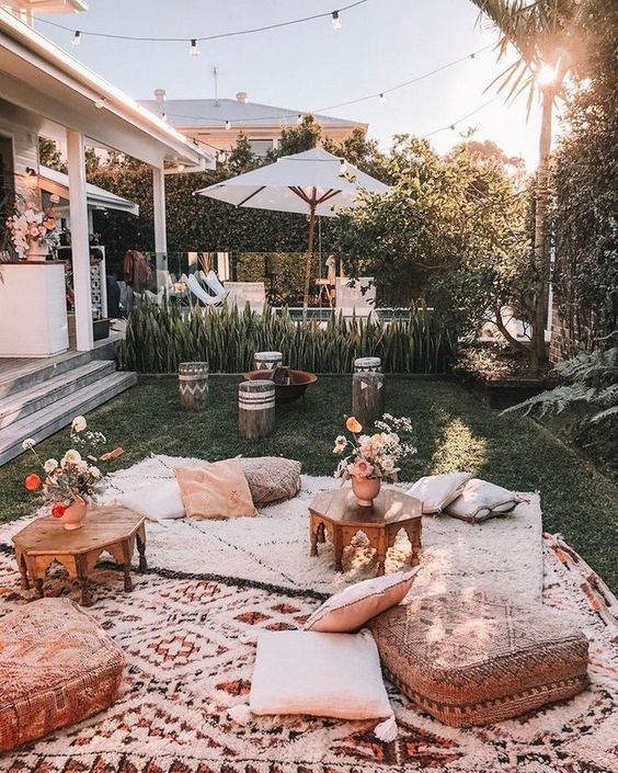 an outdoor boho space with layered neutral rugs, cushions and pillows, low carved tables, patterned stools