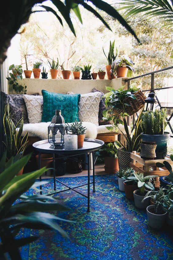 a Morocco inspired balcony with a bold blue rug, a loveseat with boho pillows, a side table, potted plants and cacti, Moroccan lanterns