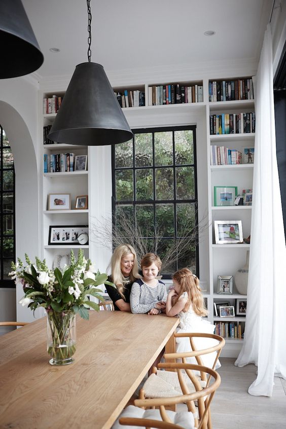 a Scandinavian dining room with built-in shelves, a wooden dining table and chairs black pendant lamps