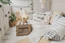 a beautiful creamy boho balcony with a low sofa with lots of pillows and blankets, a crate as a table, layered rugs and striped blankets hanging for privacy