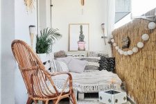 a black and white boho balcony with a low sofa with boho upholstery, bamboo, a rattan chair, a printed rug and even a portable fireplace