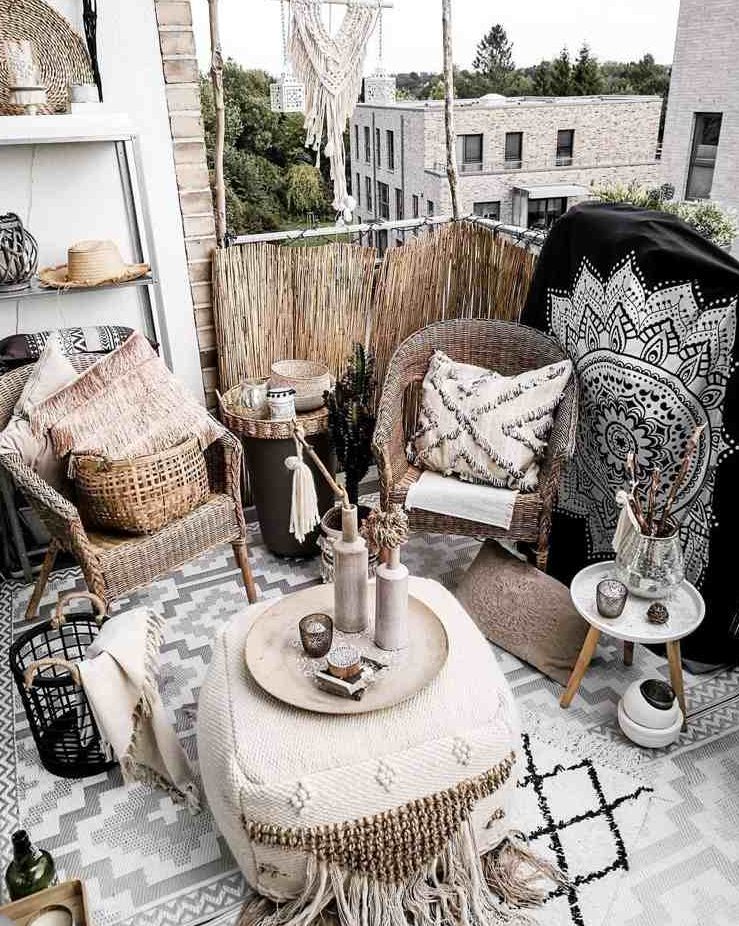 a black and white boho balcony with wicker chairs, a Moroccan pouf, a small side table, baskets and candle lanterns and beautiful Morocco inspired blankets, pillows and rugs