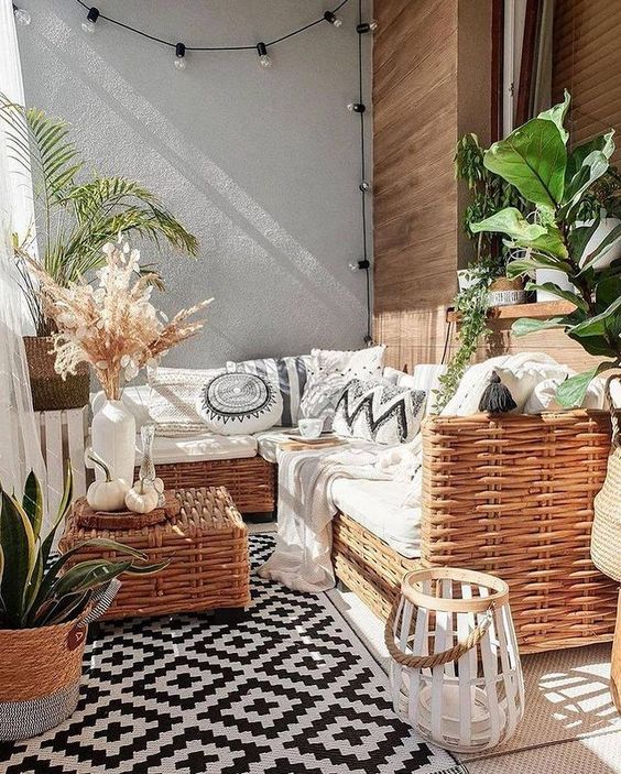 a boho balcony done in black and white, with wicker furniture, potted plants, candle lanterns and lights and black and white upholstery