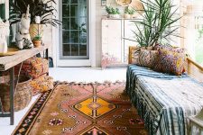 a boho porch done with a bench, a wooden console, potted plants, baskets and printed textiles plus a boho rug