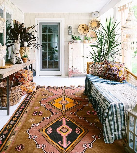 a boho porch done with a bench, a wooden console, potted plants, baskets and printed textiles plus a boho rug