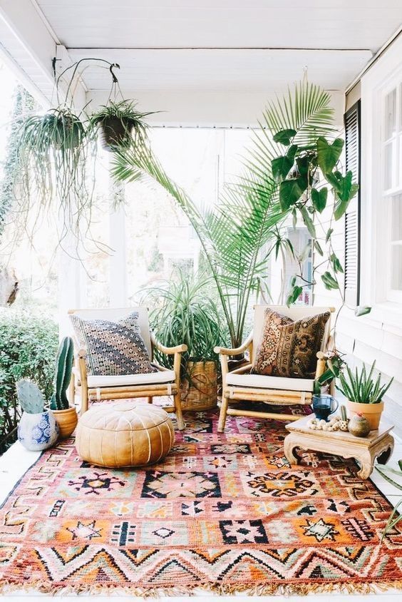 a boho porch with rattan and wooden furniture, printed textiles, potted greenery and cacti is very welcoming