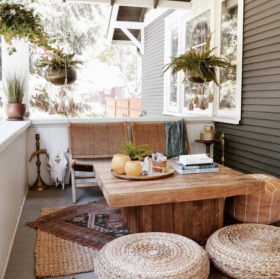a boho porch with wooven and woven furniture, boho layered rugs, potted greenery and brass touches