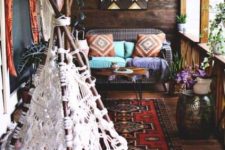 a boho porch with woven and wooden furniture, a boho rug, colorful printed textiles and a macrame teepee