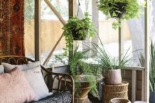 a boho screened porch with rattan furniture, a living edge table, potted greenery and boho textiles plus jute jars