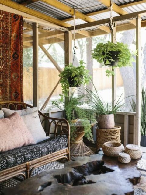 a boho screened porch with rattan furniture, a living edge table, potted greenery and boho textiles plus jute jars