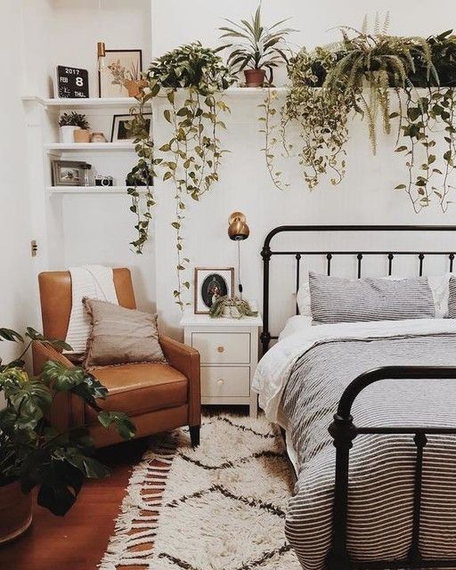 a boho spring bedroom with a metal bed, a leather chair, neutral and printed bedding, potted greenery and brass touches