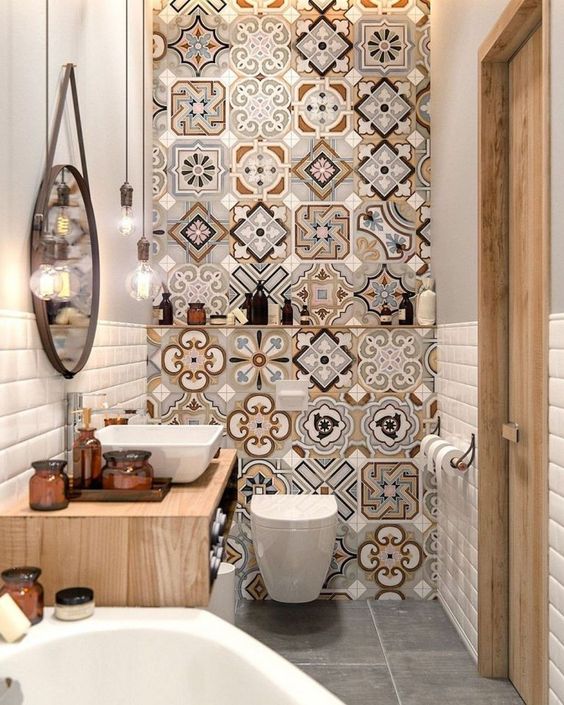 a bright and small bathroom with a mosaic tile wall, a floating wooden vanity, a tub, a round mirror and bulbs