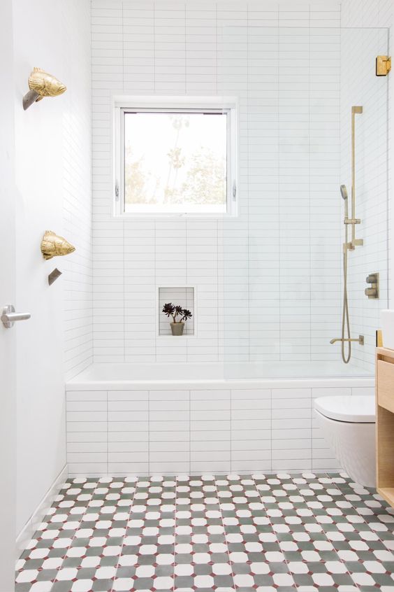 a bright bathroom with a mosaic floor, white tiles with built-in shelves, a window and gold hardware