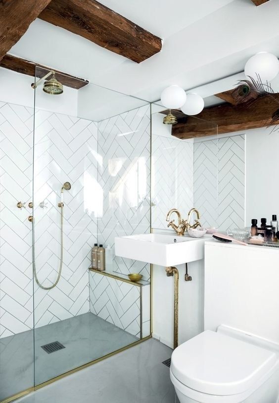 a bright glam white bathroom with chevron clad tiles, gilded touches, dark wooden beams and a square sink