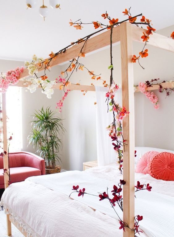 a bright spring bedroom with a wooden bed, a coral chair, faux cherry blossom covering the bed and coral pillows