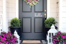 a bright spring porch done with hot pink blooms in pots,with a bright and textural floral and greenery wreath and greenery in pots