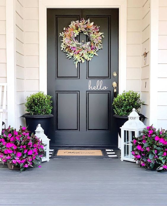 a bright spring porch done with hot pink blooms in pots,with a bright and textural floral and greenery wreath and greenery in pots