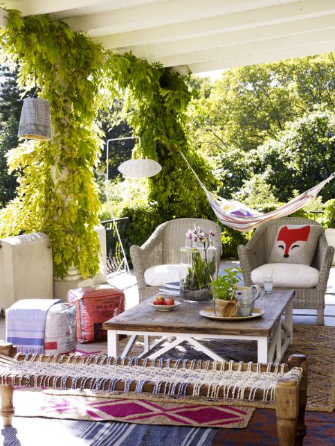 a bright spring terrace with wooden and wicker furniture, with bright textiles and lots of greenery around