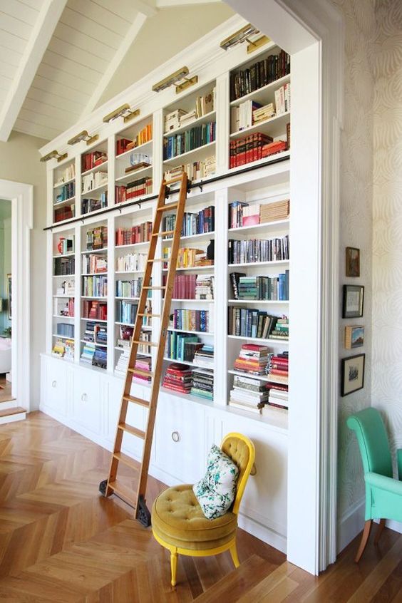 a chic built-in bookshelf unit with a ladder, a mustard chair and additional lights is very chic
