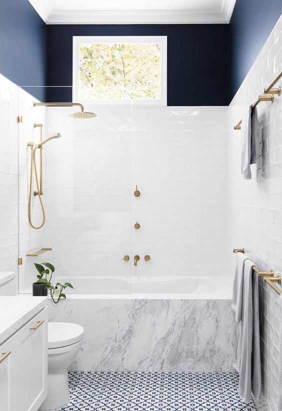 a chic contemporary bathroom with a mosaic floor, a marble clad tub, a navy toouch and gilded hardware