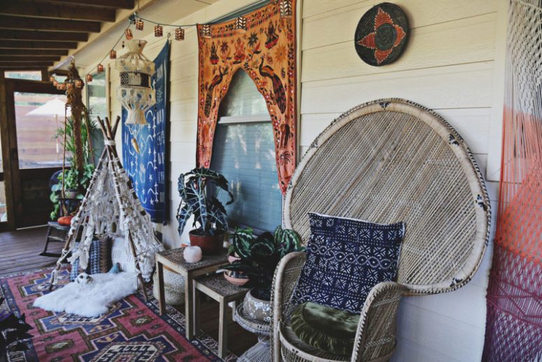 a colorful gypsy porch with a peacock chair, potted plants, printed textiles, a macrame teepee and a garland of lights