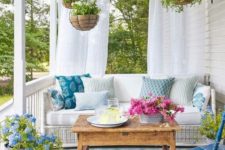 a colorful spring porch with potted greenery and blooms, printed pillows and vintage furniture