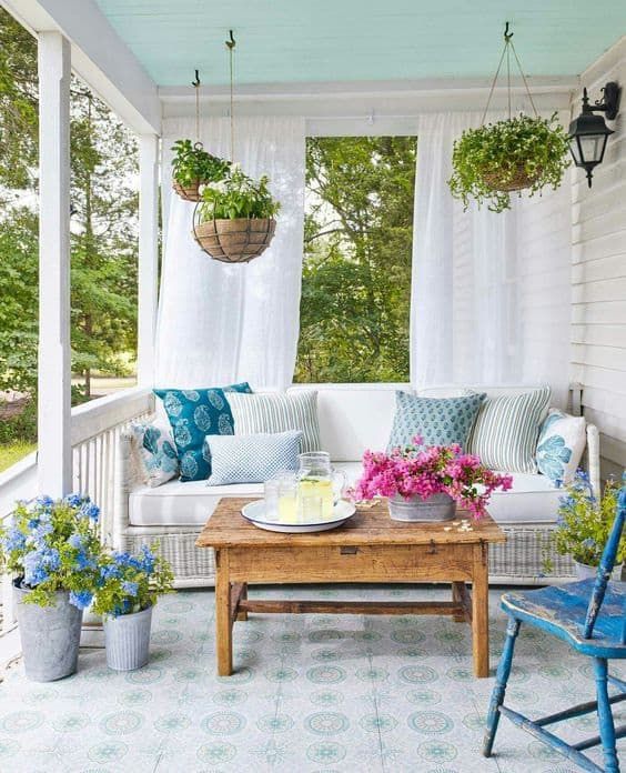 a colorful spring porch with potted greenery and blooms, printed pillows and vintage furniture