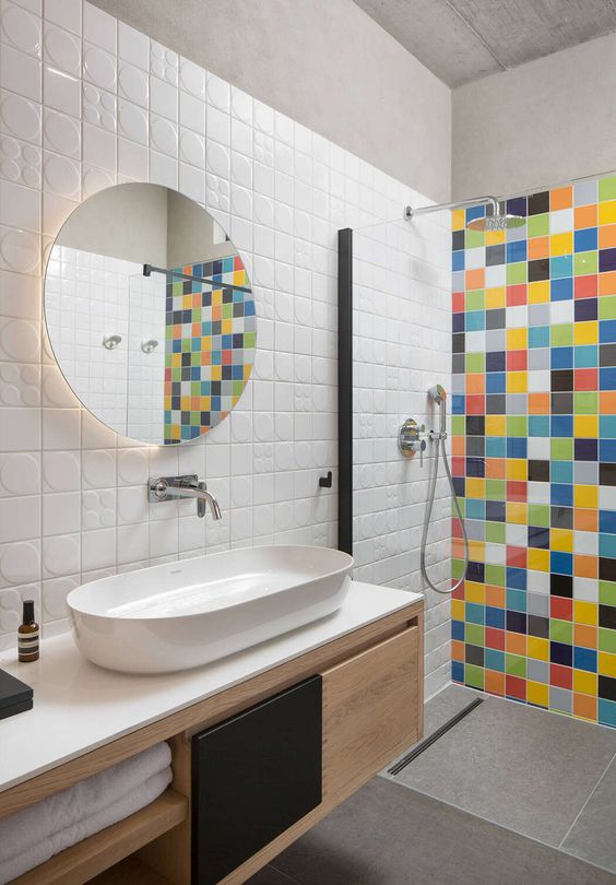 a contemporary neutral bathroom with white tiles on the walls and grey large scale ones on the floor plus a multi-color tile accent wall