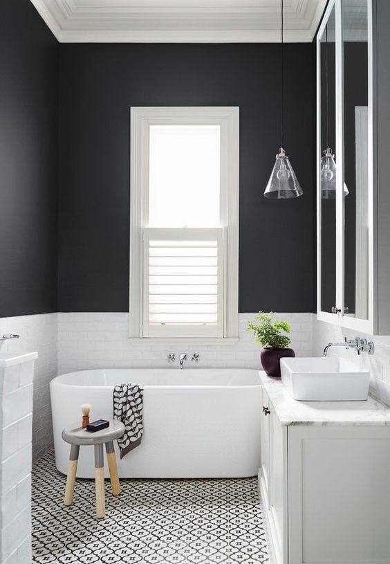 a contrasting bathroom with black and white walls, a mosaic floor, an oval tub, a stool and a glass cone pendant lamp