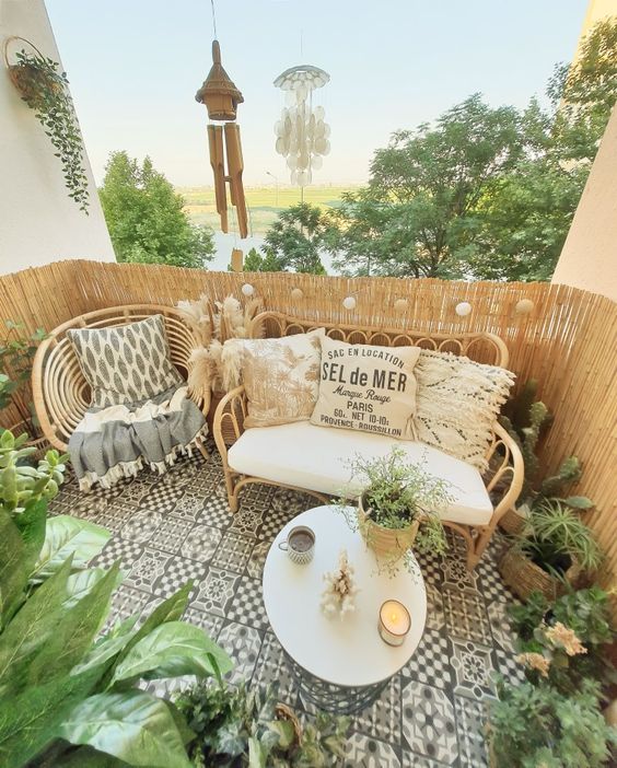 a cool boho balcony with black and white tiles, rattan furniture wiht boho pillows, potted plants and a round table with candles is cool