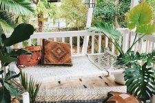 a cool boho porch with a woven hammock, printed textiles, potted greenery, candle lanterns and a wooden chest