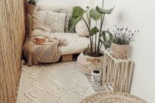 a cute boho balcony done in creamy shades, with a low seat with boho pillows, a beautiful rug, a crate and a basket with a plant, a jute pouf and some candle lanterns