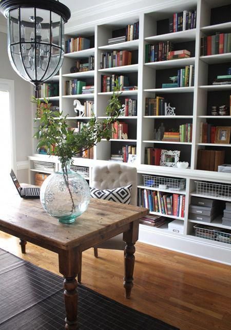 a dark built-in bookshelf with lots of books, wire baskets, greenery, figurines and other decor