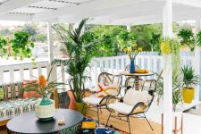 a fun boho porch with rattan chairs and a wooden sofa, colorful printed textiles, potted cacti and greenery