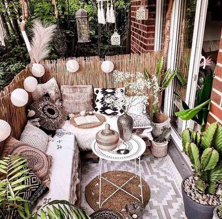 a gorgeous boho balcony with layered rugs, a corner pallet sofa with lots of boho pillows, Moroccan lanterns, lights and potted greenery is amazing